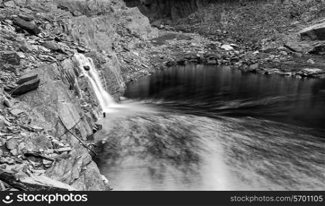 Landscape image of waterfall flowing into old abandoned quarry black and white
