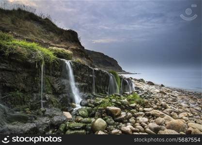 Landscape image of waterfall flowing onto rocky beach at sunrise