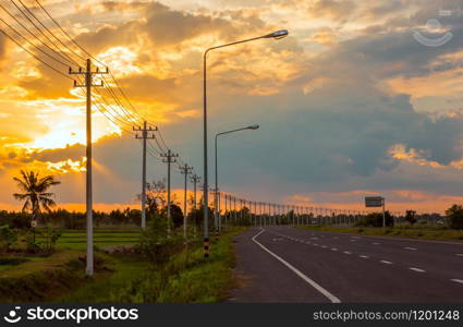 Landscape in the fields and background, orange sky, twilight and electric poles on the road