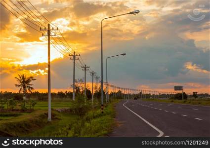 Landscape in the fields and background, orange sky, twilight and electric poles on the road