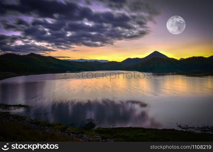 Landscape lake river nature with full moon sunset yellow and purple sky dark clouds moving on silhouette mountain background