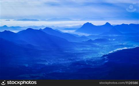 Landscape mountain with fog mist blue sky and rising sun in the morning on hill - Silhouettes blue mountain range background