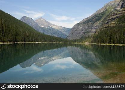 Landscape of Avalanche Lake and nearby mountains in Glacier National Park. The reflection on the lake provides a near mirror image.