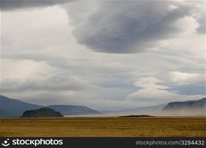 Landscape of barren meadow before mountains, with grey cloudy skies