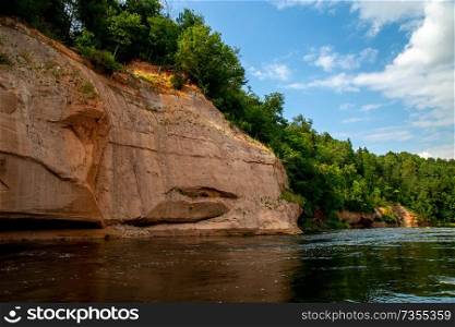 Landscape of cliff with cave near the river Gauja, blue sky and forest. Gauja is the longest river in Latvia, which is located only in the territory of Latvia. 