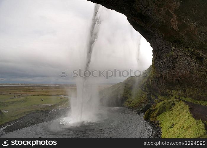 Landscape of farmland from behind water falling into a pool from a cliff