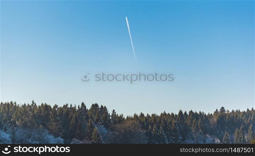 Landscape of forest against blue sky with plane trail on sunny frosty morning. Nature background. Landscape of forest against blue sky with plane trail on sunny frosty morning