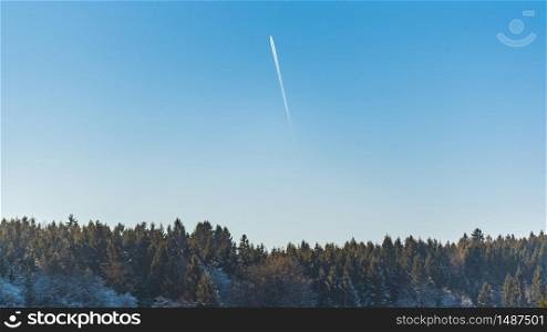 Landscape of forest against blue sky with plane trail on sunny frosty morning. Nature background. Landscape of forest against blue sky with plane trail on sunny frosty morning