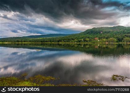 Landscape of green forest mountain and storm cloud reflect on water in rainy season
