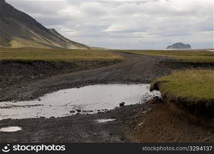 Landscape of mountain and pasture with rural dirt road and puddles