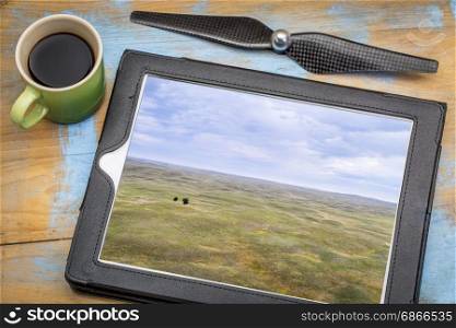 landscape of Nebraska Sandhills with two lonely trees, reviewing aerial image on a digital tablet with a cup of coffee