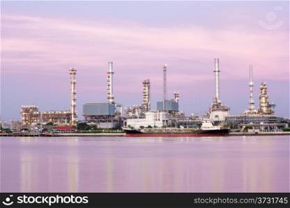 landscape of Oil refinery plant along river with tanker at dusk