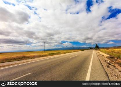 Landscape of road through golden fields with clouds, Granada Province, Spain