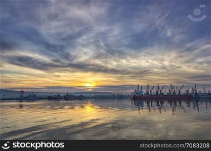 Landscape of ship and cranes in port at sunset.