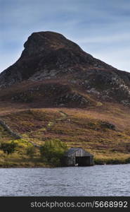 Landscape of steep hill with small boathouse on lake in foreground