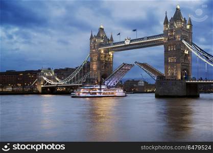 Landscape of Tower Bridge in London at twilight opening against . England, London, Tower Bridge. Tower Bridge opening against a stormy sky with a boat passing under the cantilevers.. Landscape of Tower Bridge in London opening against a stormy sky with a boat passing under the cantilevers