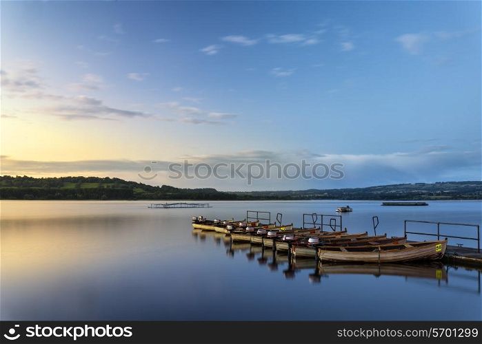 Landscape sunrise over still lake with boats on jetty