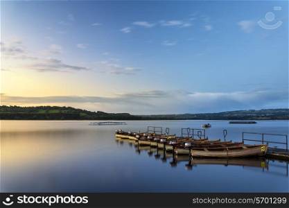 Landscape sunrise over still lake with boats on jetty