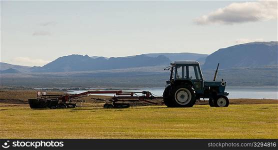 Landscape, tractor pulling farm machinery before rugged mountain