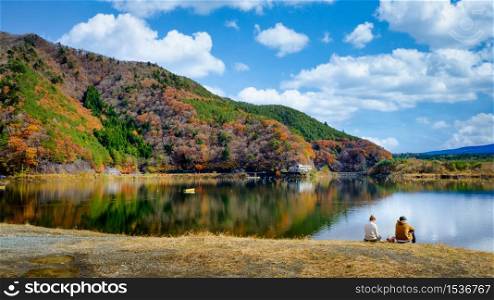 landscape view autumn leaves of Kawaguchiko Lake and couple sitting by the river in japan