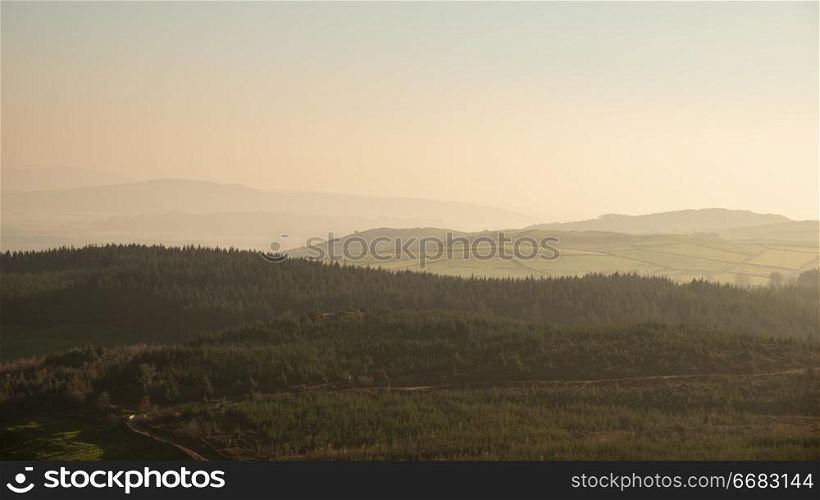 Landscape view from Gummers How in Lake District over beautiful Autumn Fall color forest with hazy unlight in late afternoon
