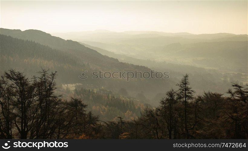 Landscape view from Gummers How in Lake District over beautiful Autumn Fall color forest with hazy unlight in late afternoon