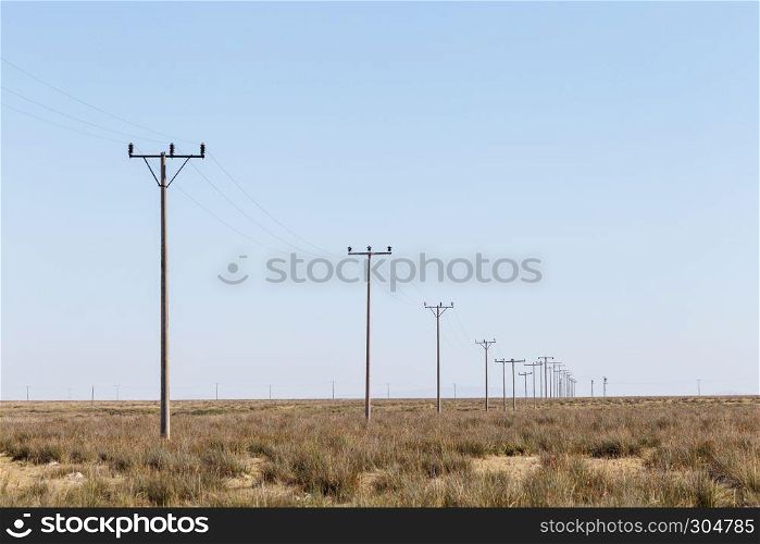 Landscape view of many power poles in a row on meadow with blue sky on background.. Landscape view of many power poles in a row