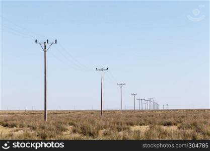 Landscape view of many power poles in a row on meadow with blue sky on background.. Landscape view of many power poles in a row