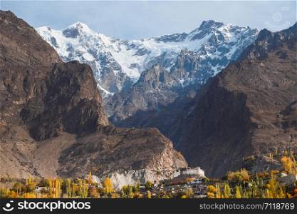 Landscape view of snow capped Ultar Sar mountain in Karakoram range with ancient Baltit fort and foliage in autumn in Karimabad. Hunza valley, Gilgit Baltistan, Pakistan.