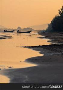 Landscape view of water along the beach with orange afernoon sky over sea. Fishing boat on beach with reflection, Thailand