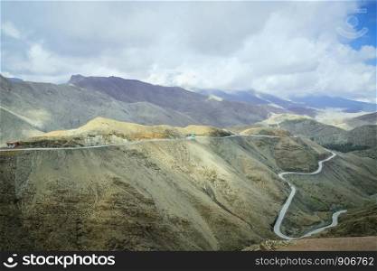 Landscape view of winding road along the Atlas mountain range against cloudy blue sky, Morocco.