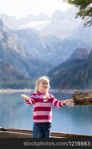 landscape with a beautiful mountain lake. girl drinks water from wooden water trough at the autumn mountains