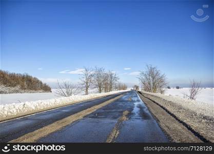 Landscape with a road in the winter with melted snow. The concept of winter travel by car.