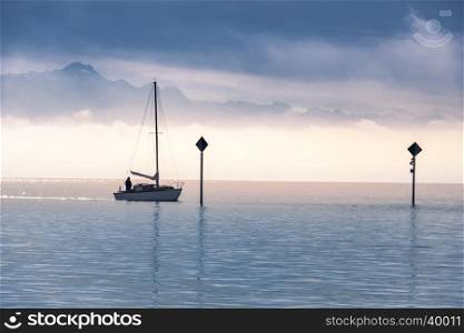 Landscape with a single boat sailing on the Bodensee lake and the Alps mountains covered with mist at the horizon, in the morning light.