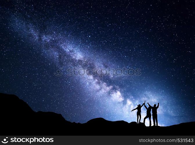 Landscape with blue Milky Way. Night starry sky with silhouette of a happy family with raised-up arms on the mountain. Beautiful Universe. Space background