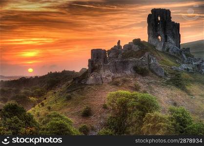 Landscape with castle ruins on hill and vibrant beautiful sunrise in distance