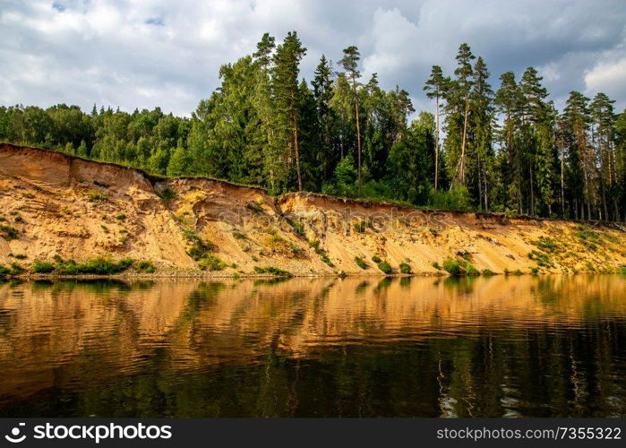 Landscape with cliff near the river Gauja, sky and trees reflection in water. The Gauja is the longest river in Latvia, which is located only in the territory of Latvia. 