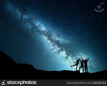 Landscape with colorful green Milky Way. Night starry sky with silhouette of a sporty happy family with raised-up arms on the mountain. Beautiful Universe. Space background