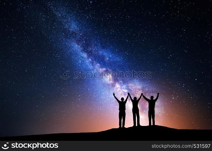 Landscape with colorful Milky Way and silhouette of a happy family with raised-up arms on the mountain. Night starry sky with yellow light. Beautiful Universe. Space background