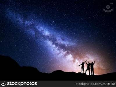 Landscape with colorful Milky Way and yellow light. Night starry sky with silhouette of a sporty happy family with raised-up arms on the rock. Beautiful Universe. Space background