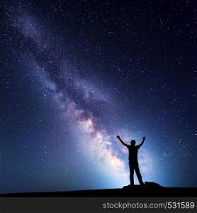 Landscape with colorful Milky Way. Night sky with stars and silhouette of a happy man with raised up arms on the mountain. Beautiful Universe. Space background