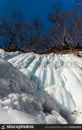 Landscape with frozen blue icicles on the river cliff wall, sunny day on the river bank. Winter season. Landscape with frozen blue icicles on the river cliff wall, sunny day on the river bank.