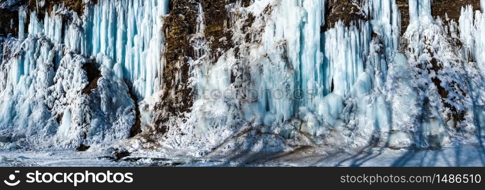 Landscape with frozen blue icicles on the river cliff wall, sunny day on the river bank. Winter season. Landscape with frozen blue icicles on the river cliff wall, sunny day on the river bank.