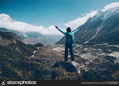 Landscape with happy girl, mountains, blue sky with clouds. Standing young woman with backpack and raised up arms on the hill and looking on mountains. Landscape with happy girl, mountains, blue sky with clouds in autumn in Nepal. Travel. Trekking in Himalayas