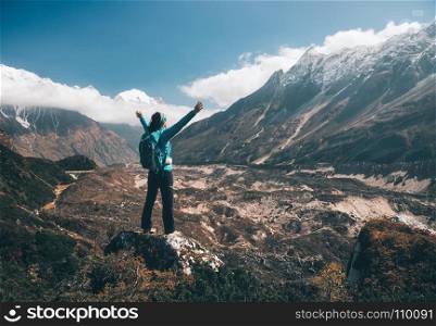 Landscape with happy girl, mountains, blue sky with clouds. Standing young woman with backpack and raised up arms on the hill and looking on mountains. Landscape with happy girl, mountains, blue sky with clouds in autumn in Nepal. Travel. Trekking in Himalayas