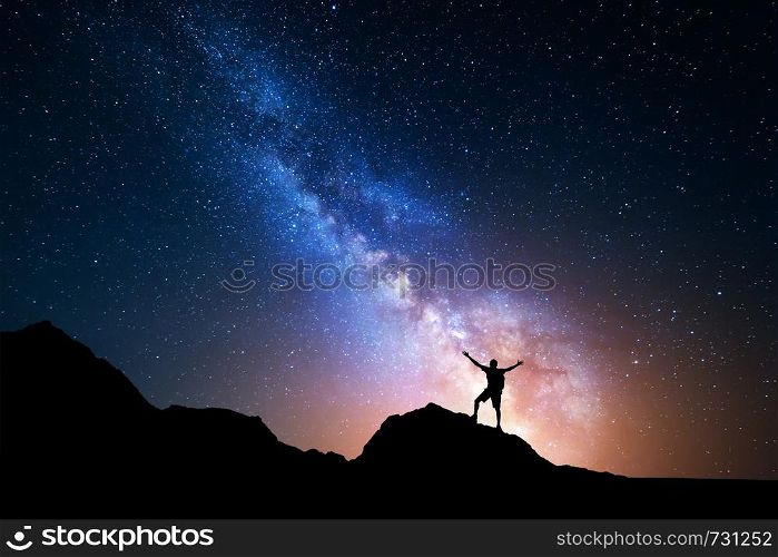 Landscape with Milky Way. Night sky with stars and silhouette of a standing happy man with raised up arms on the mountain.