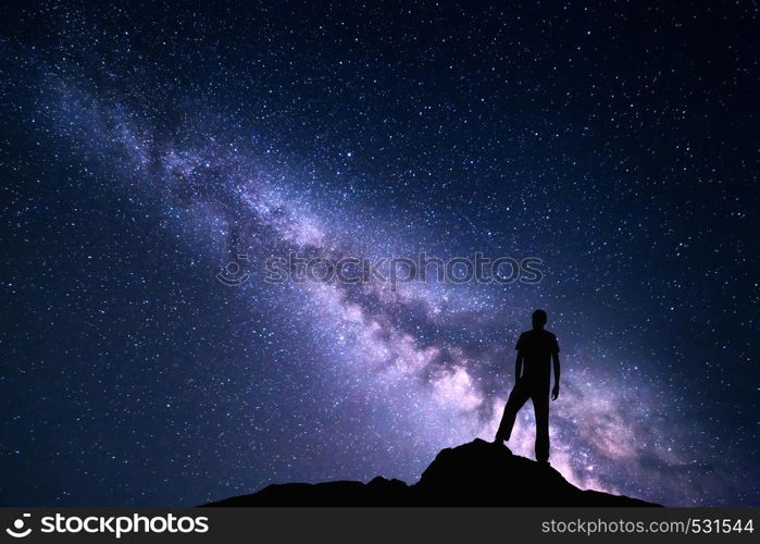 Landscape with purple Milky Way. Night sky with stars and silhouette of a happy man on the stone. Beautiful Universe. Space background