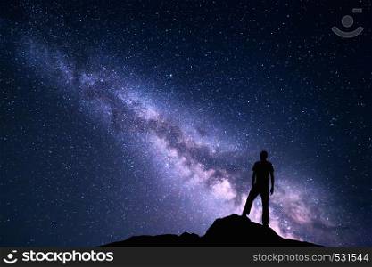 Landscape with purple Milky Way. Night sky with stars and silhouette of a happy man on the stone. Beautiful Universe. Space background