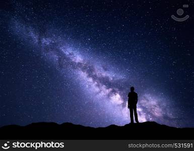 Landscape with purple Milky Way. Night sky with stars and silhouette of a happy man on the mountain. Beautiful Universe. Space background