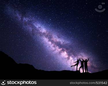 Landscape with purple Milky Way. Night starry sky with silhouette of a happy family with raised-up arms on the mountain. Beautiful Universe. Space background